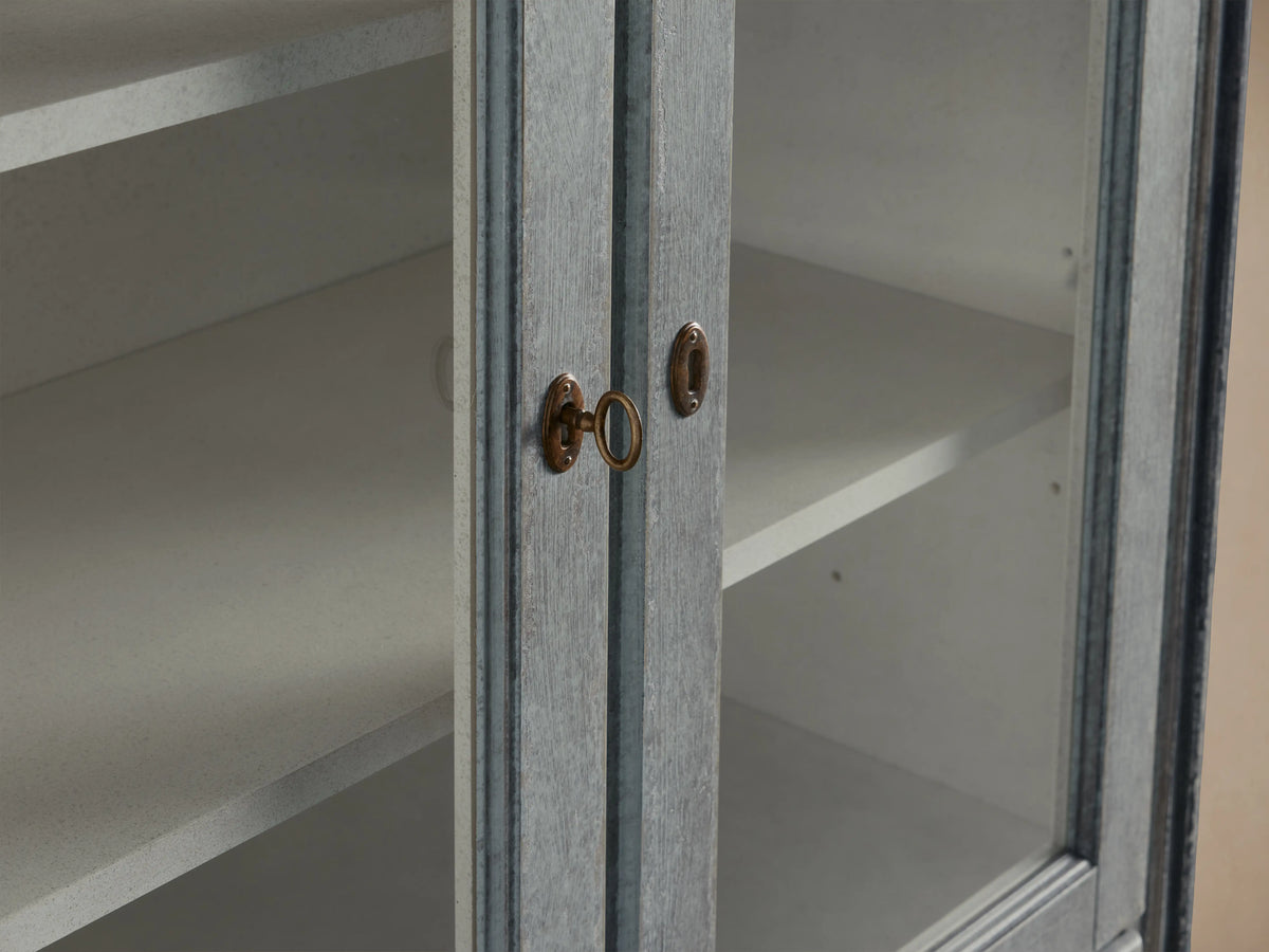 Close-up of the Giotto Cabinet showing antique blue finish, brass handles, and partial view of interior shelving with a weathered look.