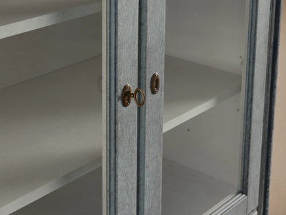 Close-up of the Giotto Cabinet showing antique blue finish, brass handles, and partial view of interior shelving with a weathered look.
