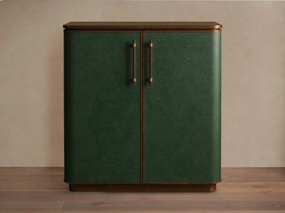 The Grant Bar, crafted from walnut wood and green faux leather with brass handles, stands on a wooden floor against a neutral wall.