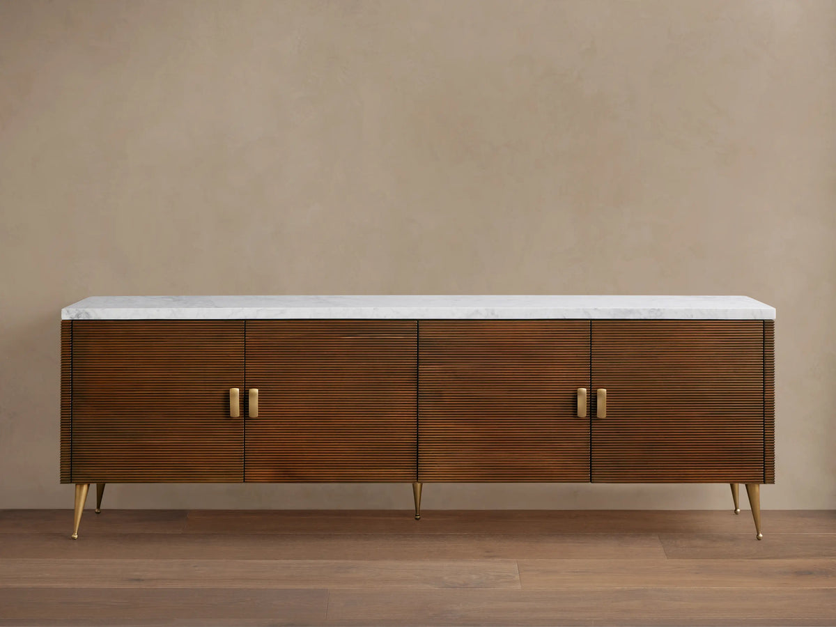 Giselle Media Console: Long dark mahogany console with reeded doors, white marble top, brass bar handles, and tapered legs.