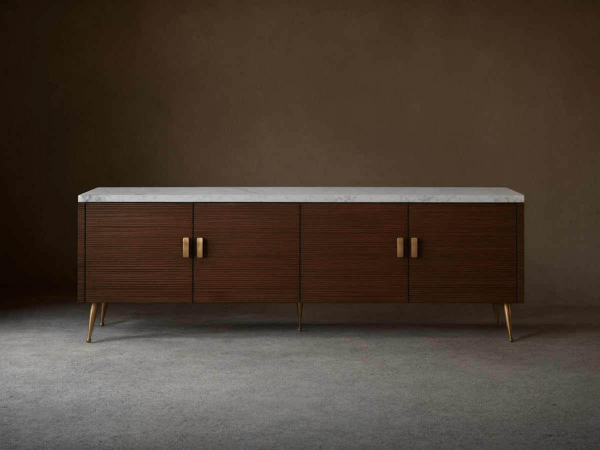 Giselle Media Console: Long dark mahogany console with reeded doors, white marble top, brass bar handles, and tapered legs.