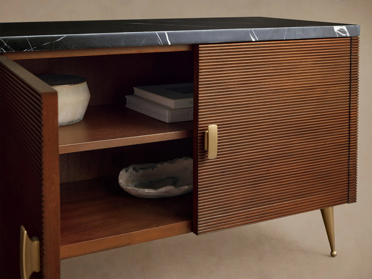 Giselle Media Console: dark mahogany wood with reeded doors & black marble top. Brass handles. Right doors open, revealing interior shelves.