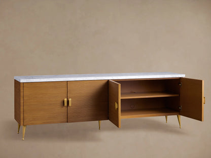 Giselle Media Console with reeded warm brown doors, white marble top, and brass handles and legs, against a tan wall.