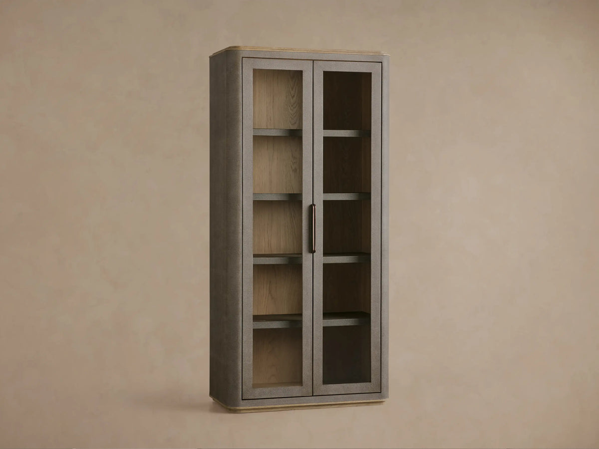 Close-up of Harrow Cabinet's dark faux shagreen door with bronze handle, revealing interior shelves and decorative items.
