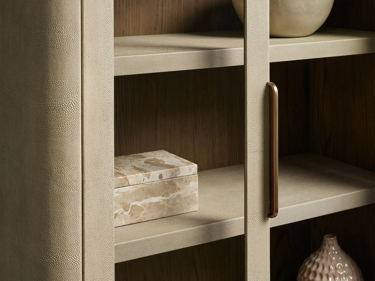 Harrow Cabinet: Light beige faux shagreen cabinet with rounded edges, two glass doors, a brass handle, and four interior shelves.