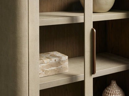 Harrow Cabinet: Light beige faux shagreen cabinet with rounded edges, two glass doors, a brass handle, and four interior shelves.