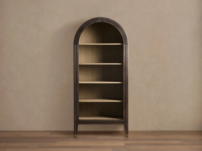 Arched Hattie Bookcase made of oak wood with shiplap back panel, adjustable shelves, and brass-capped feet on a wooden floor.