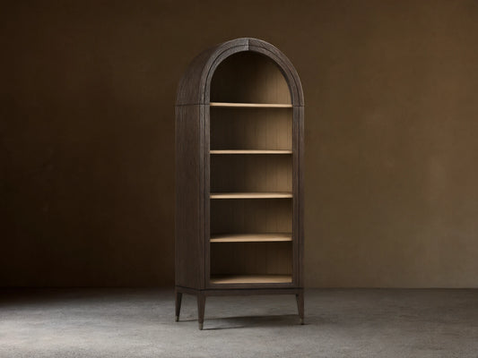 Arched Hattie Bookcase made of oak wood with shiplap back panel, adjustable shelves, and brass-capped feet on a wooden floor.
