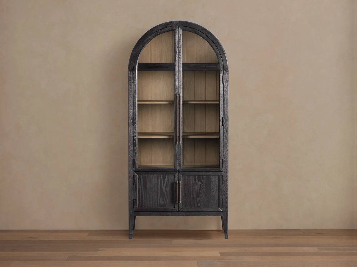 Front view of the Dark Hattie Glass Cabinet with an arched top, glass doors, light shiplap back panel, and reeded hardware.