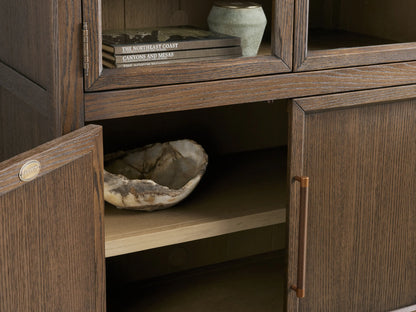Hattie Squared Glass Cabinet in dark ebony wood, arched glass doors with lighter interior shelves, solid lower doors, bronze reeded handles.
