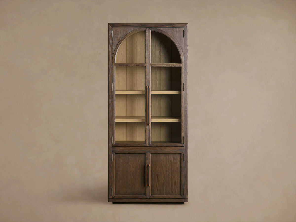 Hattie Squared Glass Cabinet, close-up. Open dark oak door, brass hinge, light interior shelf with marbled bowl. Right, closed door with bronze pull.