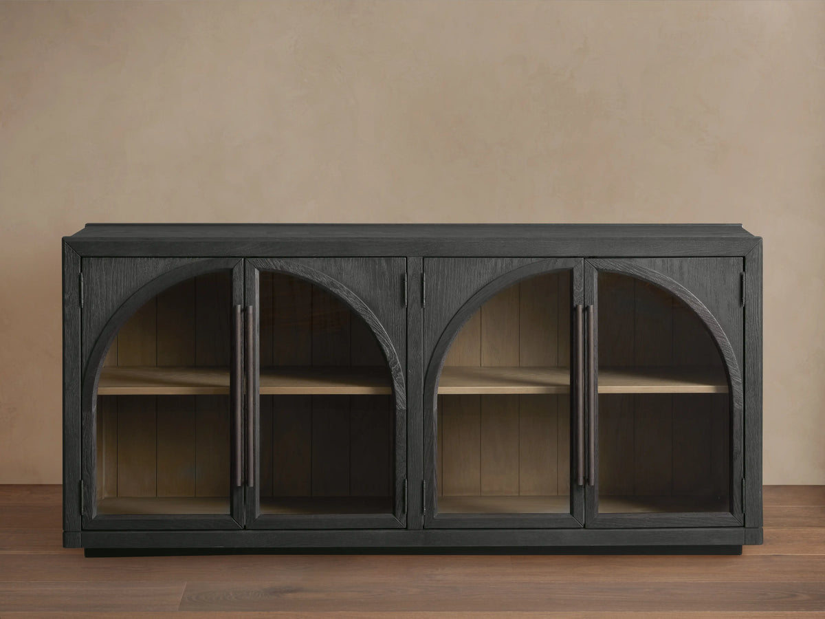 Hattie Sideboard made of dark oak with arched glass doors, showing interior shelves and shiplap back paneling against a neutral wall.