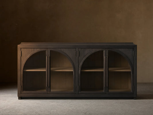 Hattie Sideboard made of dark oak with arched glass doors, showing interior shelves and shiplap back paneling against a neutral wall.