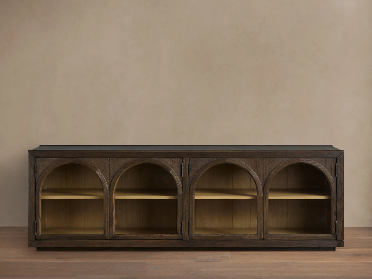 Hattie Media Console in dark oak with three arched doors, each revealing two shelves, against a beige wall. Shiplap back paneling visible.
