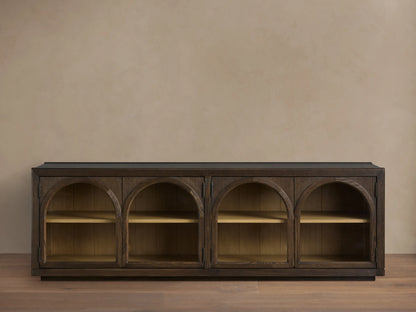 Hattie Media Console in dark oak with three arched doors, each revealing two shelves, against a beige wall. Shiplap back paneling visible.