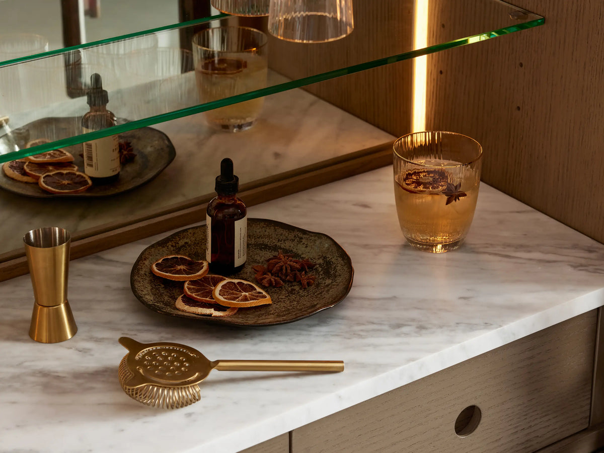 Hattie Bar Cabinet: Bahasa Brown oak, arched, glass doors show lit mirrored interior, marble surface, hanging glasses. Left door open.