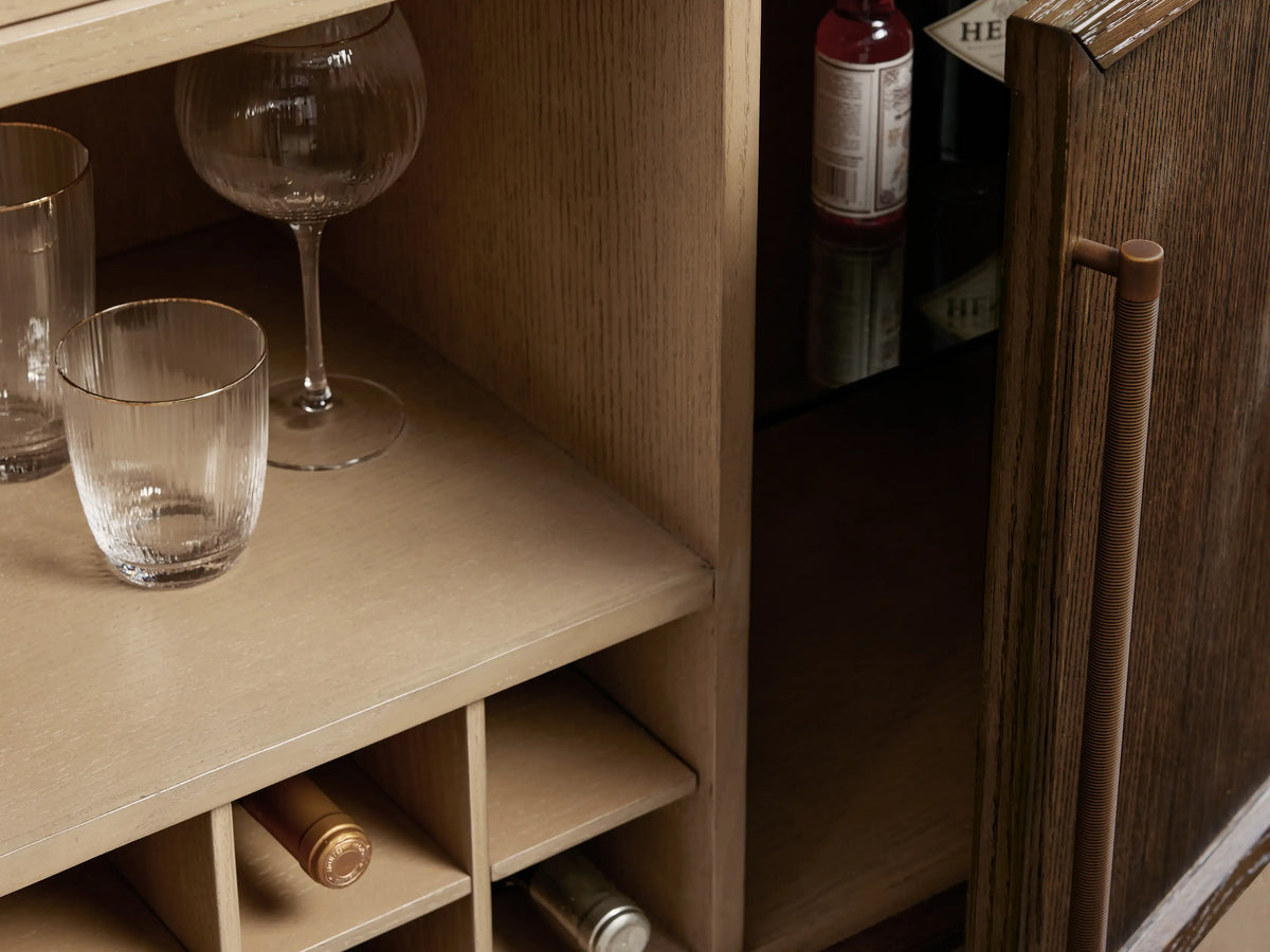 Close-up of Hattie Bar Cabinet's Carrara marble work surface with a drink, brass bar tools, and garnishes, reflecting in the mirror.