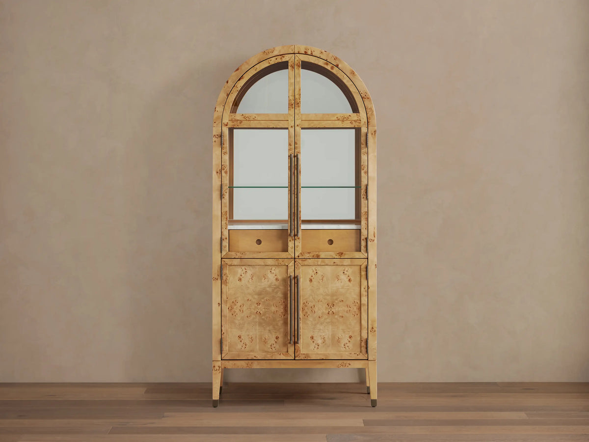 Hattie Burl Bar Cabinet, light mappa burl wood with arched top, glass doors revealing barware, and solid lower doors with brass hardware.