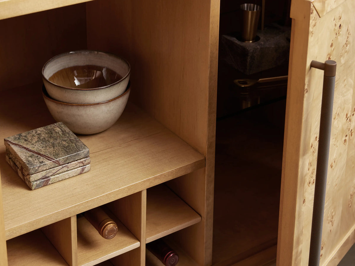 Hattie Burl Bar Cabinet's marble surface with bar tools, cherries, a cocktail, and a warm LED light reflection.