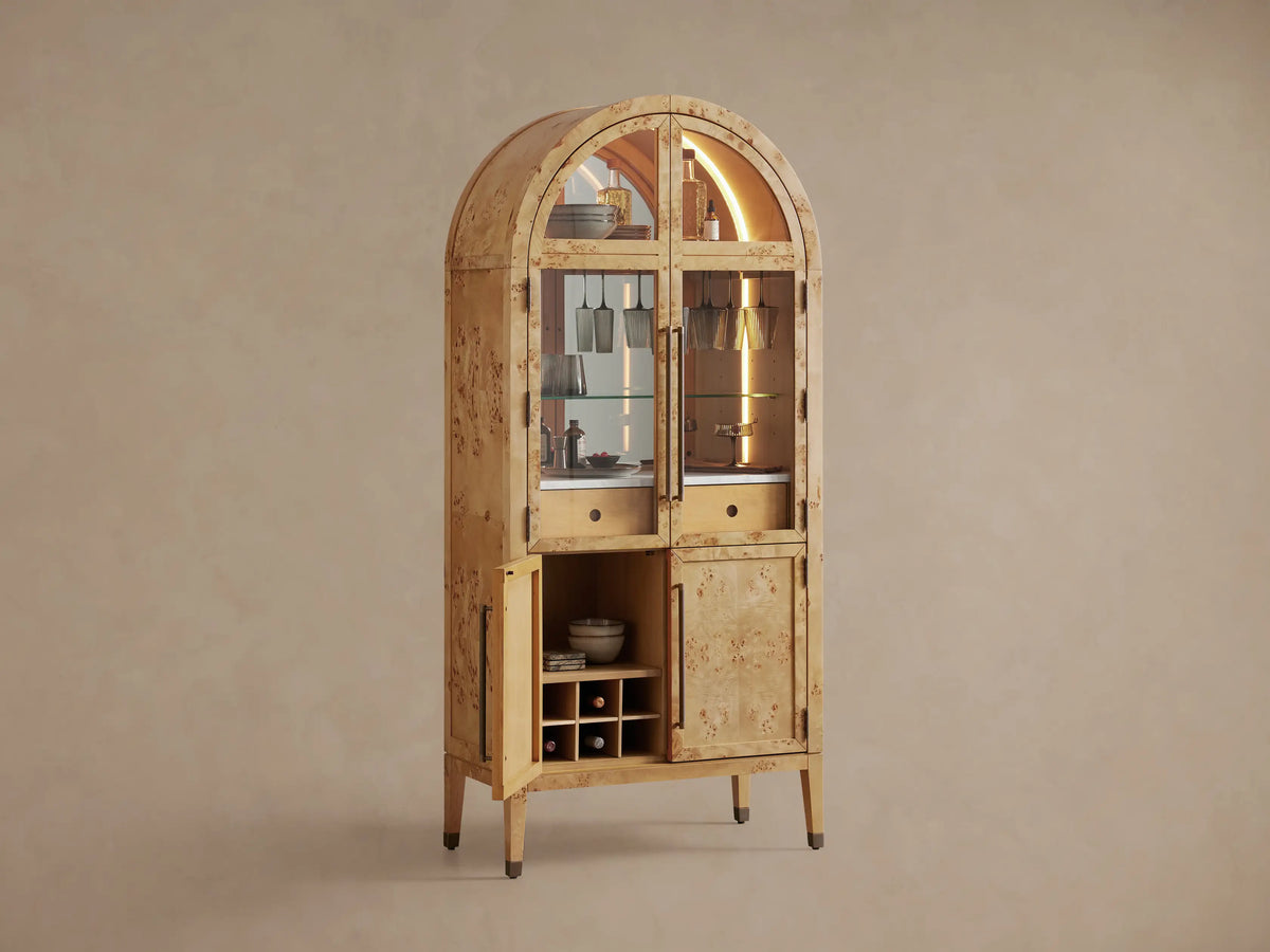 Hattie Burl Bar Cabinet's interior: light wood shelf, bottle, and dark stemware hanging from a metal rack, warmly lit.