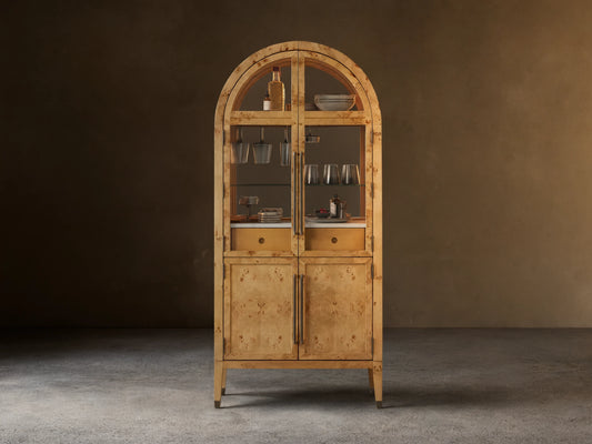 Hattie Burl Bar Cabinet, light mappa burl wood with arched top, glass doors revealing barware, and solid lower doors with brass hardware.