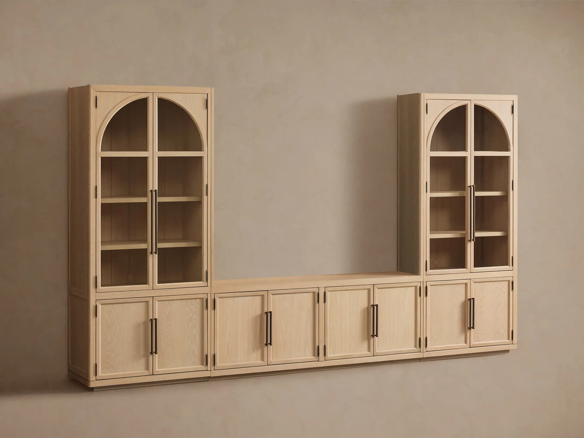 Light oak Hattie Glass Media Cabinet: two tall arched-top glass units with lower cabinets, flanking a low console, on wood floor.