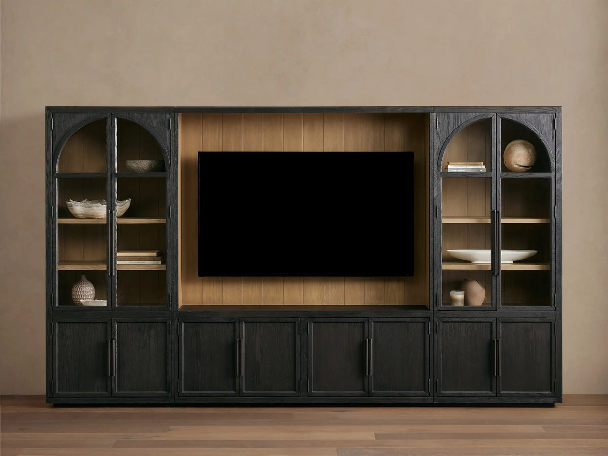 Front view of the dark Hattie Wall Unit, featuring a large TV in the center, flanked by glass-doored cabinets with arched tops and lighter shiplap back panels.
