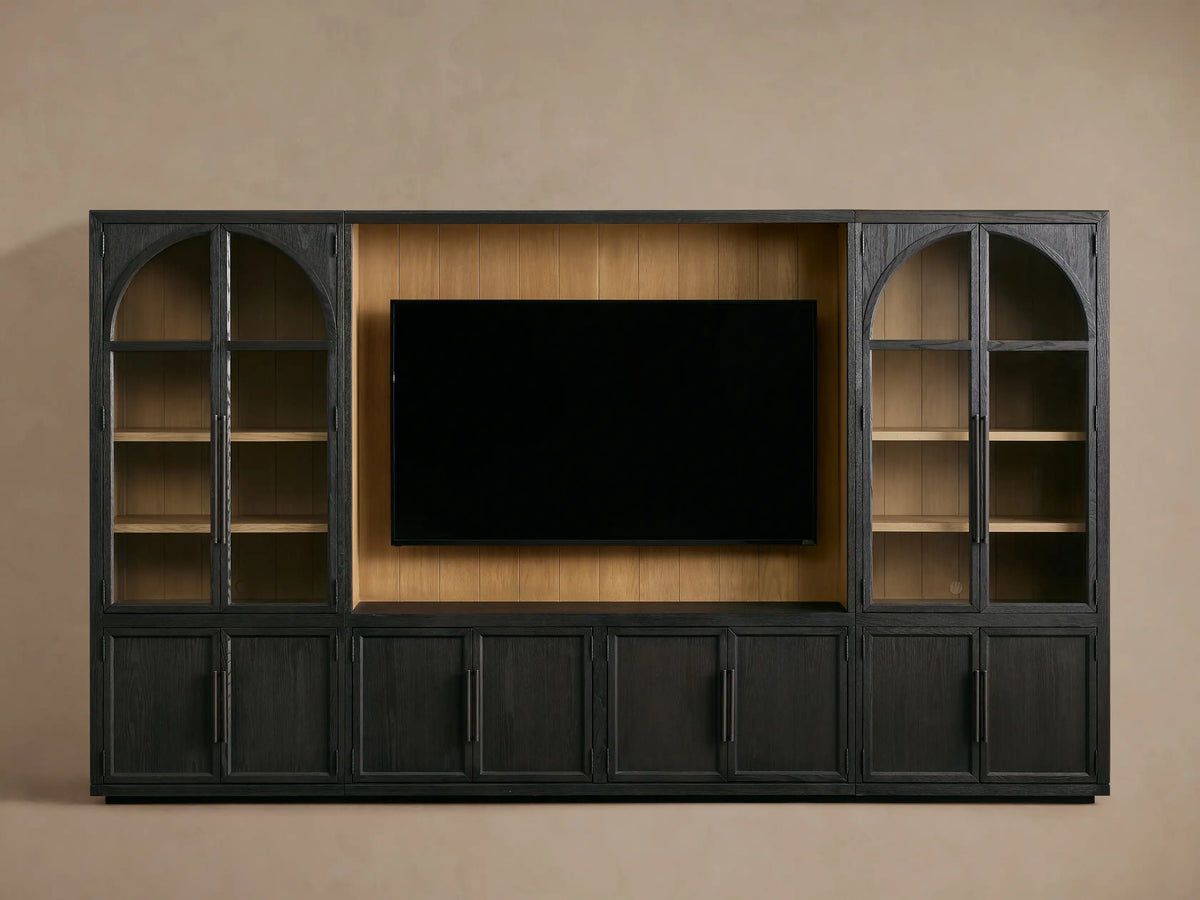 Front view of the dark Hattie Wall Unit, featuring a large TV in the center, flanked by glass-doored cabinets with arched tops and lighter shiplap back panels.