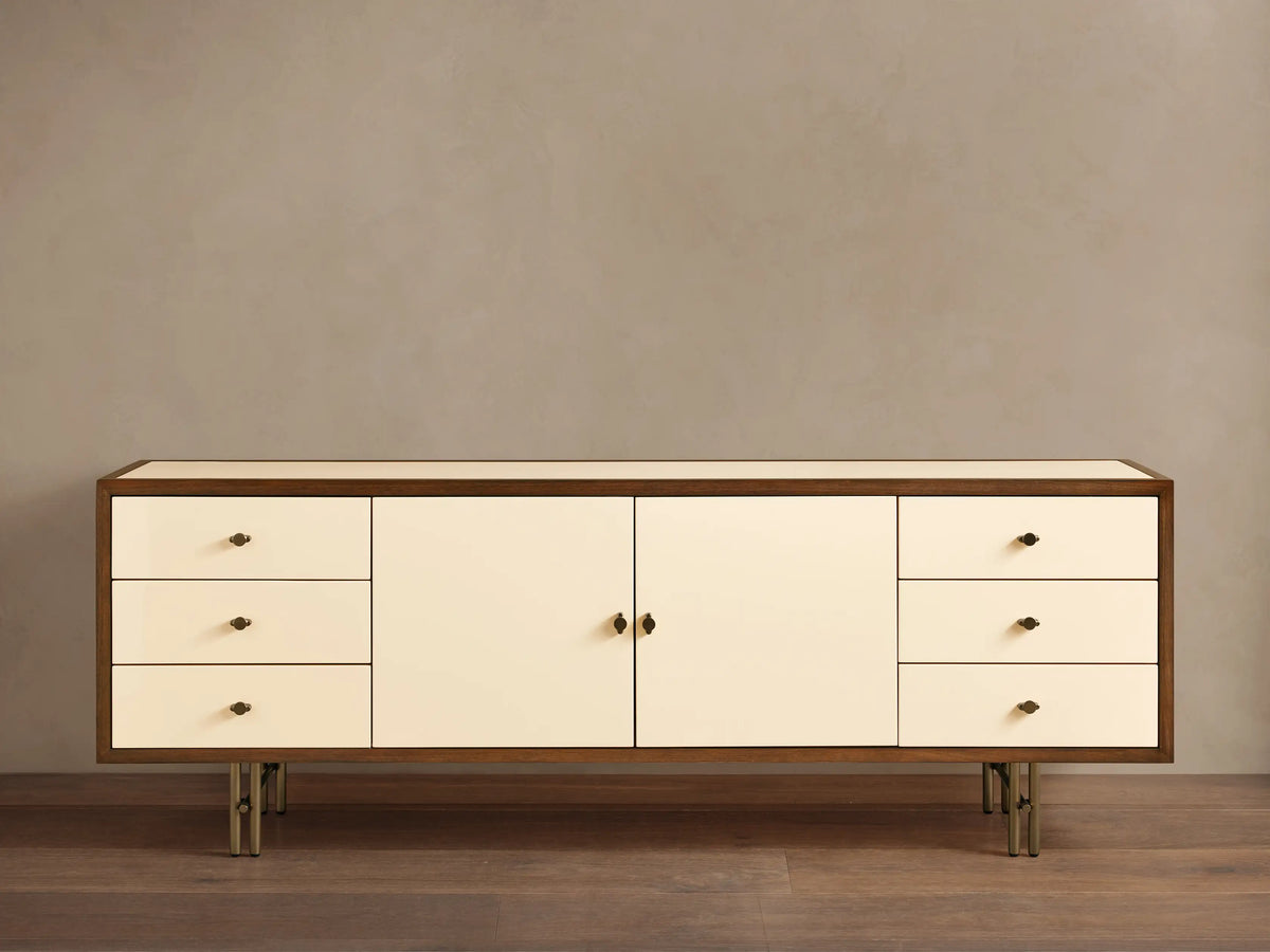 Henton Media Console in a rectangular shape with a wooden frame and cream-colored front. Features two central doors and three drawers on each side.