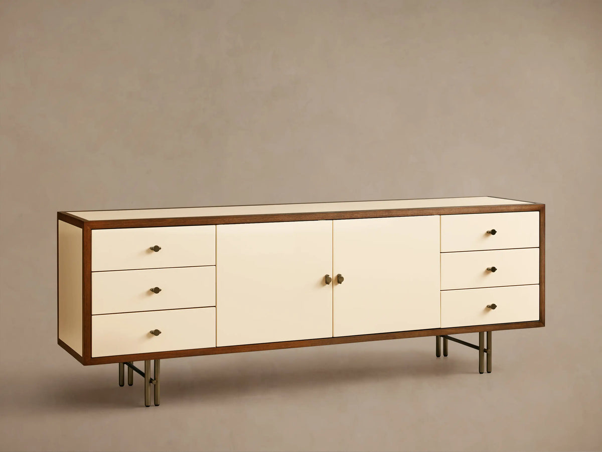 Henton Media Console in a rectangular shape with a wooden frame and cream-colored front. Features two central doors and three drawers on each side.
