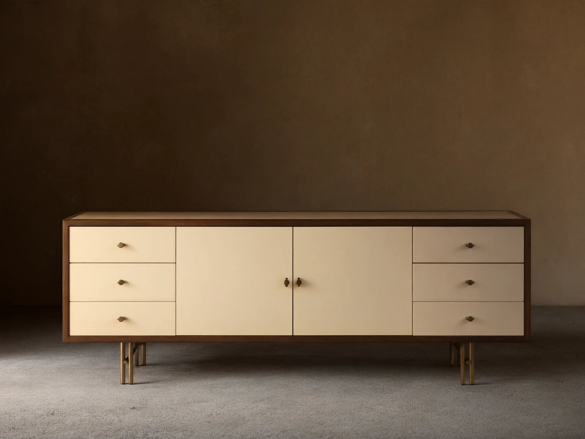 Henton Media Console in a rectangular shape with a wooden frame and cream-colored front. Features two central doors and three drawers on each side.