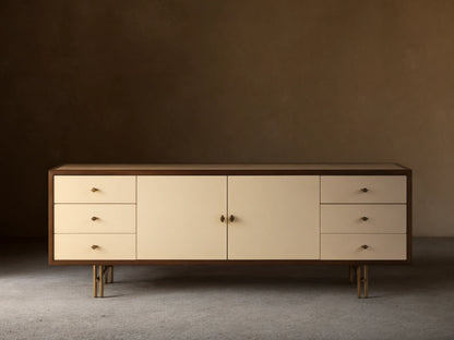 Henton Media Console in a rectangular shape with a wooden frame and cream-colored front. Features two central doors and three drawers on each side.
