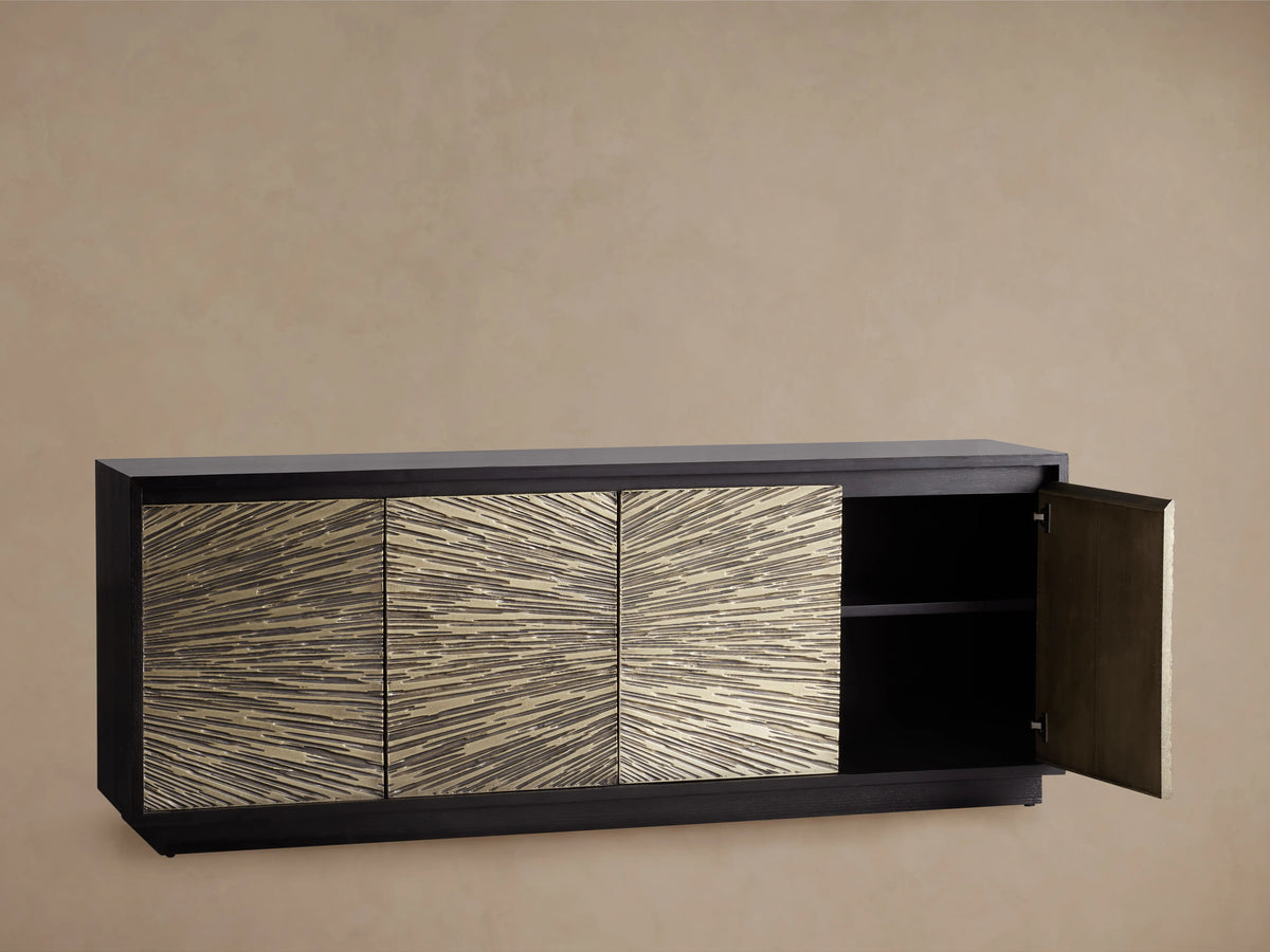 Open Helios Sideboard door with textured brass sheeting, revealing interior shelving. Dark ebony stained wood contrasts with brass pattern.
