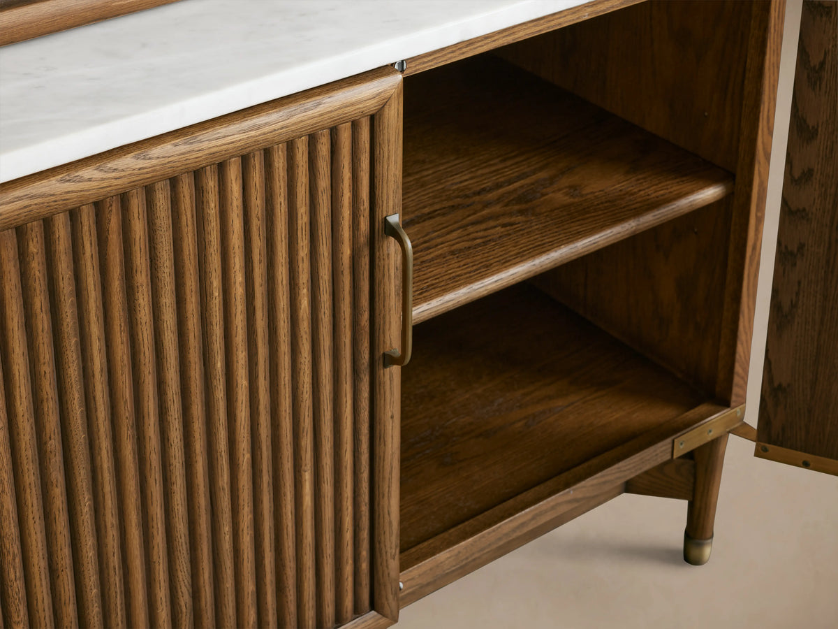 Henderson Cabinet with wood finish and Italian Carrara marble top. Open door reveals two wooden shelves inside, fluted design on door.