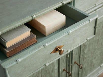 Distressed light green Iris Hall Chest with bamboo framing. Two drawers with bronze pulls, right cabinet door open revealing shelves.