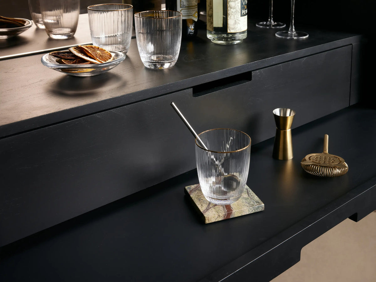Mareta Bar Cabinet features a bold, abstract gold and black design. Inside, it displays a bottle and crystal glasses on black shelves.
