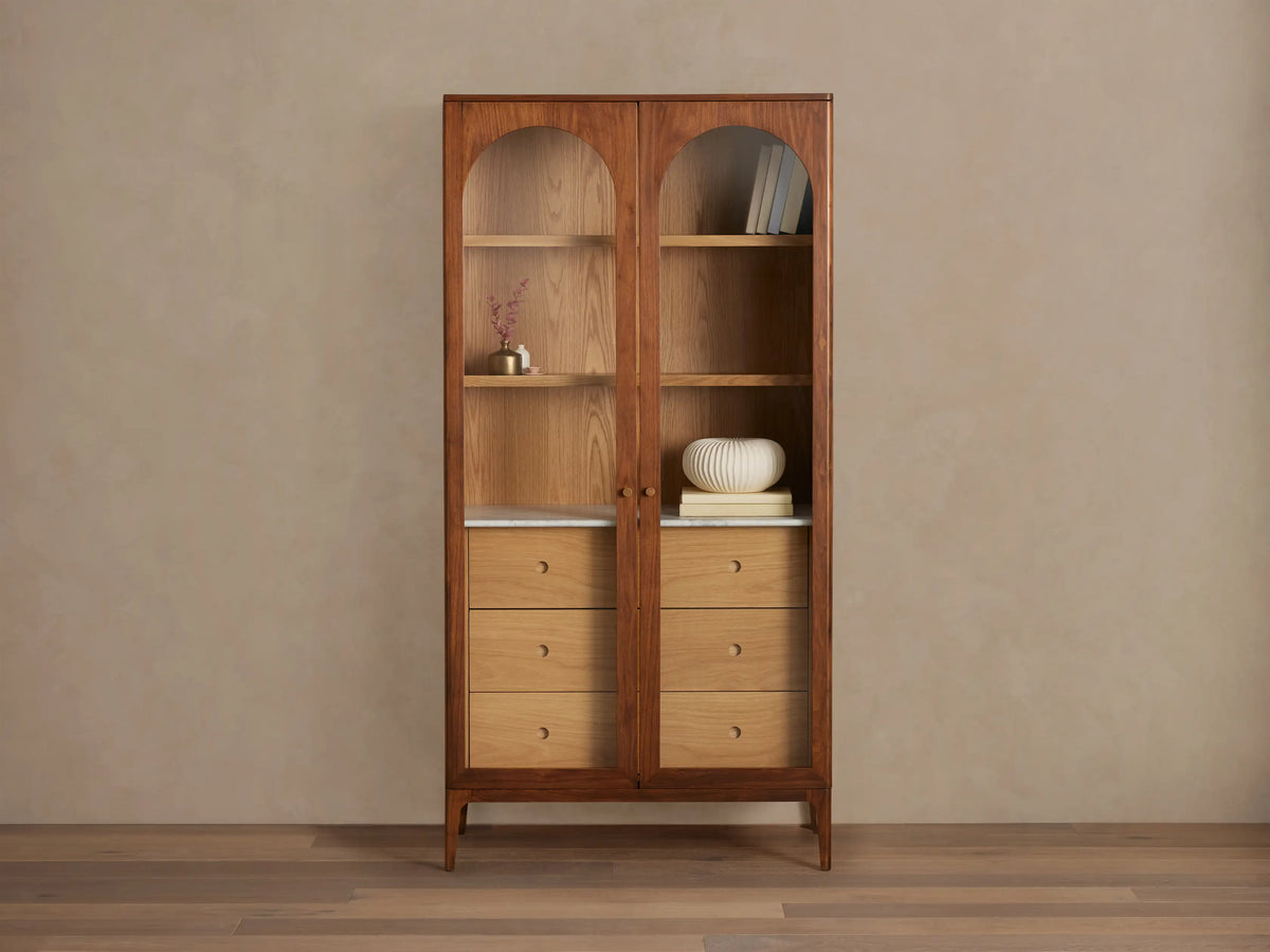 Linley Glass Cabinet with walnut finish, featuring brass knob pulls, adjustable shelves, and three drawers on a Carrara stone surface.