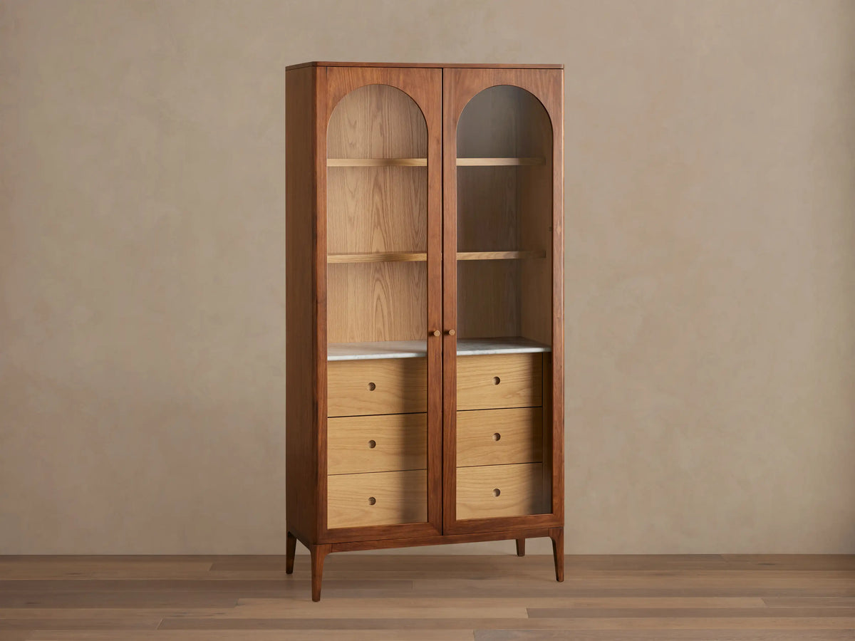 Linley Glass Cabinet with walnut finish, featuring brass knob pulls, adjustable shelves, and three drawers on a Carrara stone surface.