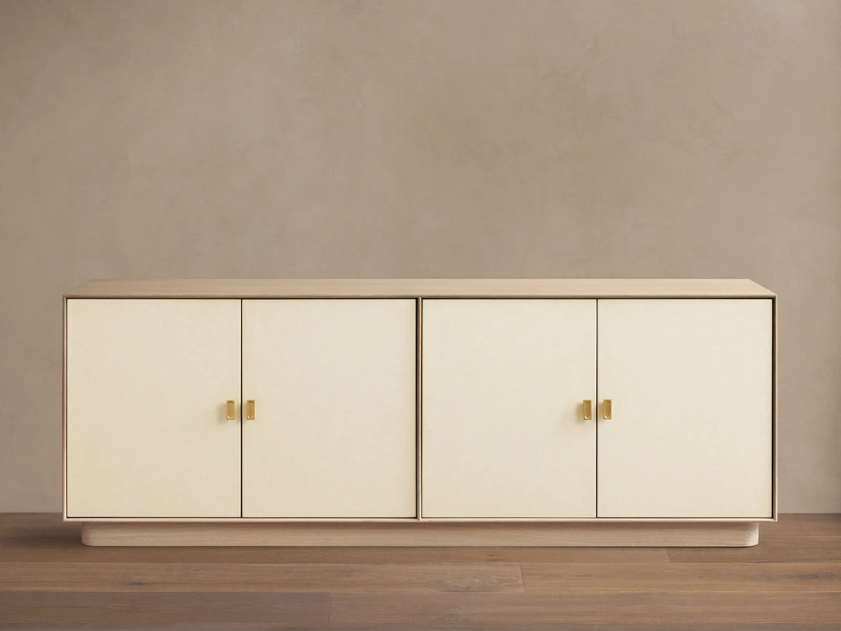 Front view of a long cream credenza with four doors, light wood top and base, and brass rectangular pull handles.