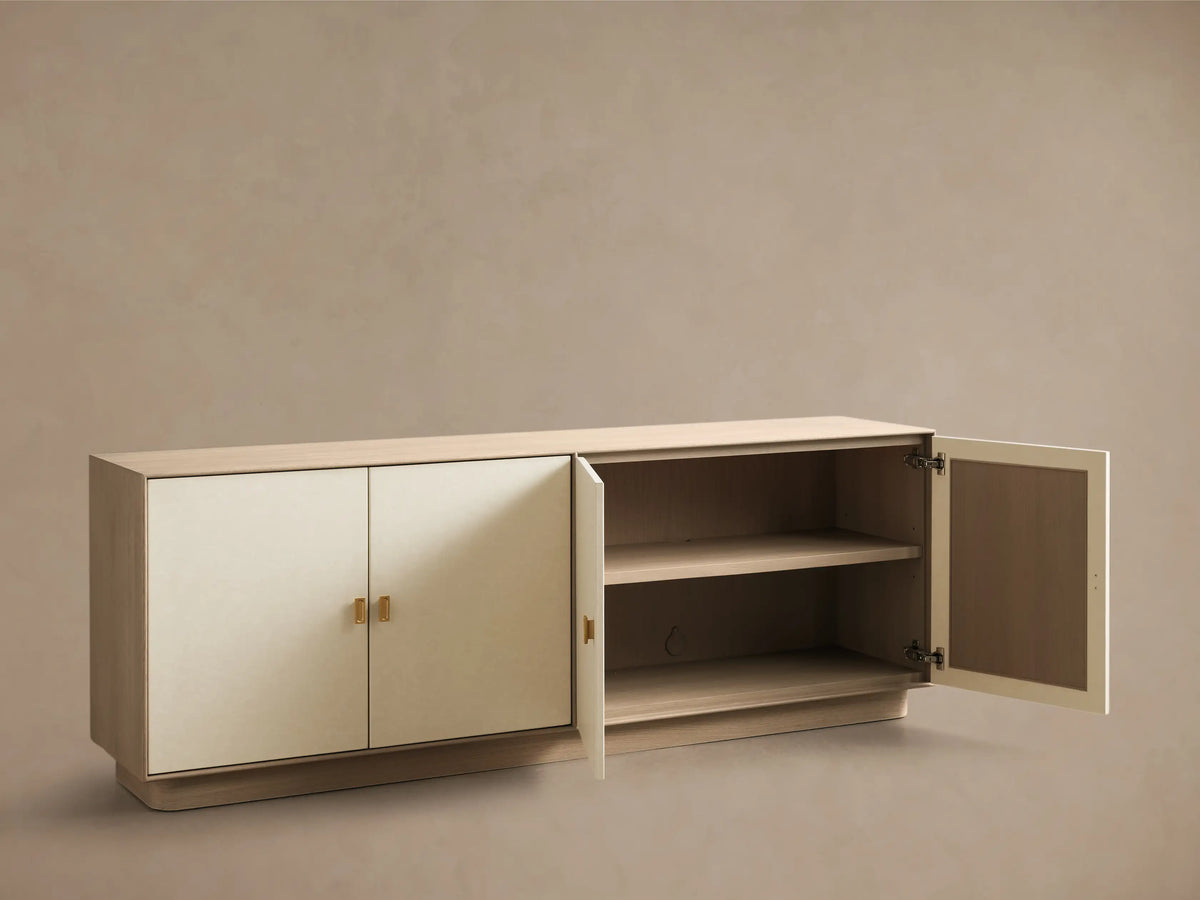 Front view of a long cream credenza with four doors, light wood top and base, and brass rectangular pull handles.
