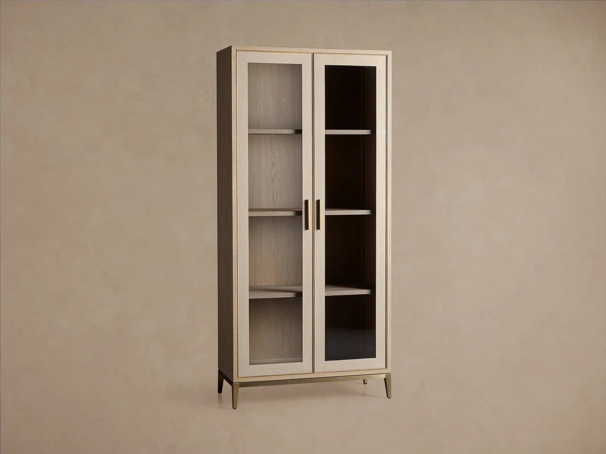 Malone Glass Cabinet: Light oak wood frame, two clear glass doors, brass handles, three shelves, and slender gold legs.
