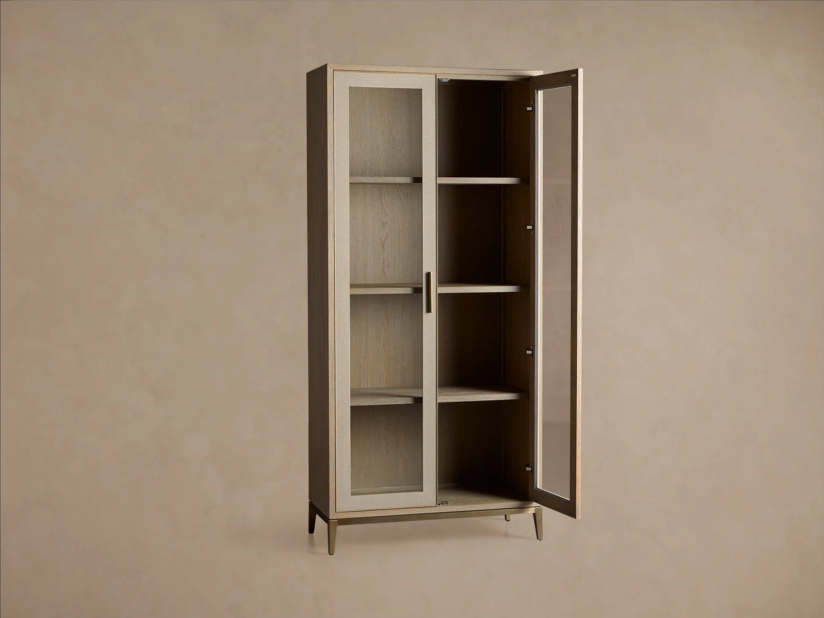Malone Glass Cabinet close-up. Light wood shelves with visible grain, textured light leather panel, vertical brass handle.