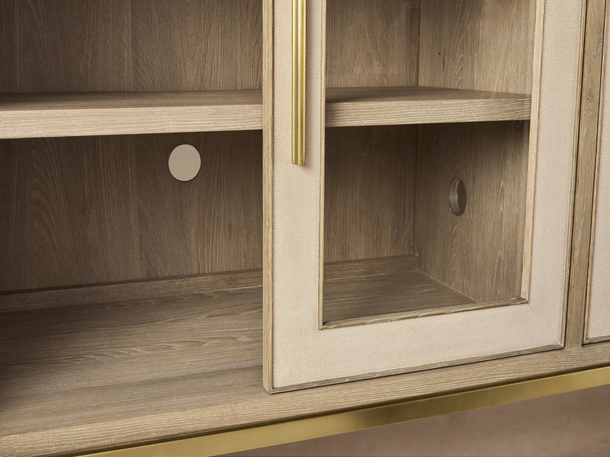 Close-up of Malone Sideboard's upper right corner. Light wood top, cream shagreen panels, metallic gold handles, and glass doors.