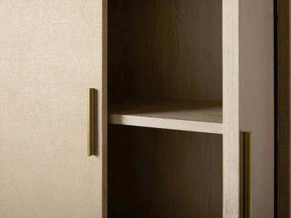 Malone Cabinet, tall, rectangular with two light, textured doors, dark handles, and gold metallic legs, on a plain wall.