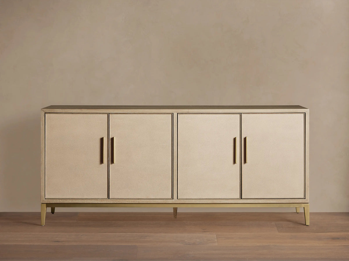 Malone Sideboard in a light shade, featuring four shagreen-textured doors with gold vertical handles, on a matching metallic base.