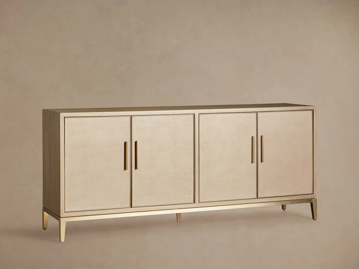 Malone Sideboard in a light shade, featuring four shagreen-textured doors with gold vertical handles, on a matching metallic base.