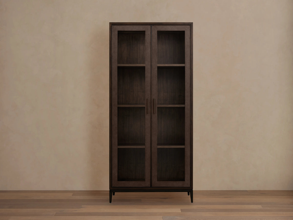 Malone Glass Cabinet in dark walnut finish with dual tempered glass doors, three shelves, and metallic handles, against a beige wall.