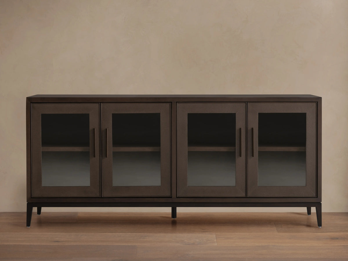 Malone Sideboard in dark walnut, featuring four glass doors, sleek handles, and visible interior shelves, on a wood floor.