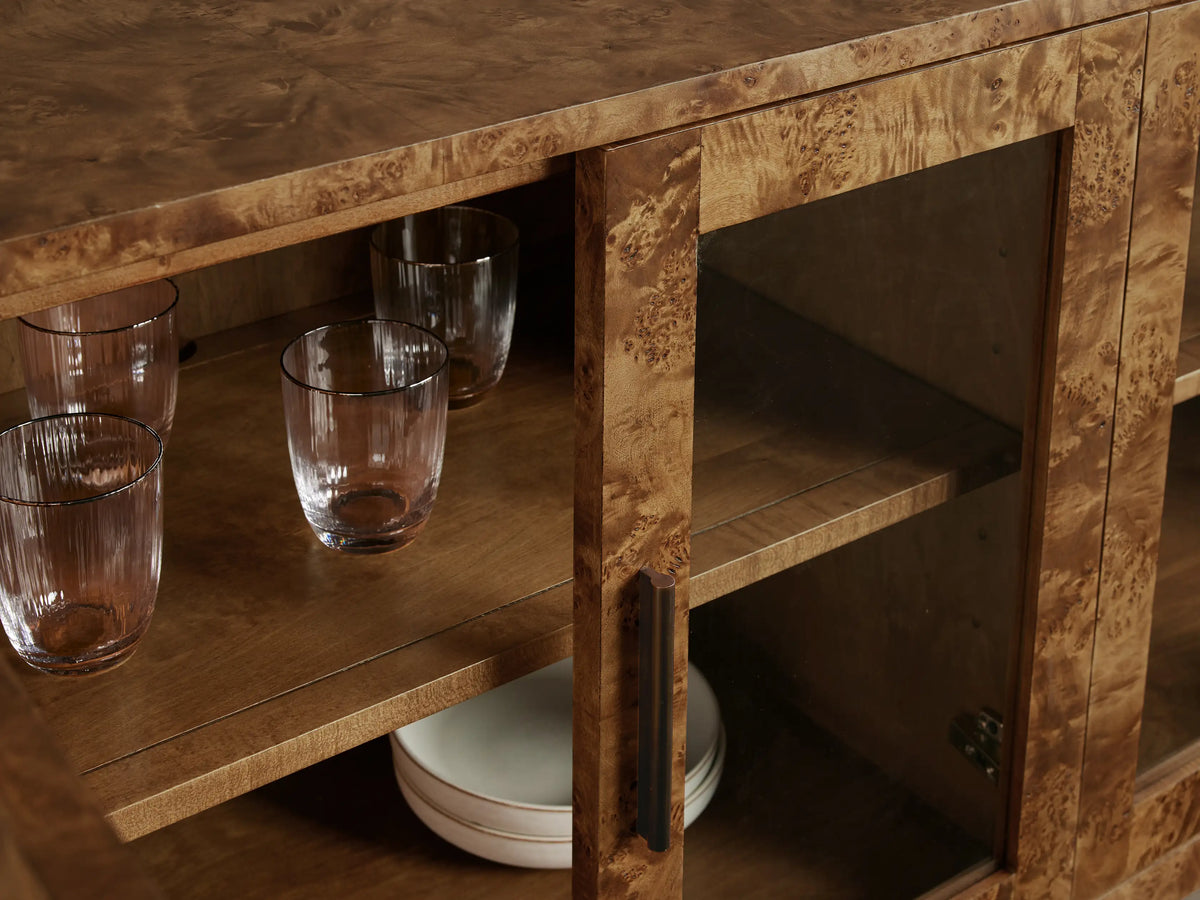 Front view of the mappa burl wood Mogadore Sideboard. Four glass doors, brass handles. Shelves display white bowls and glasses.