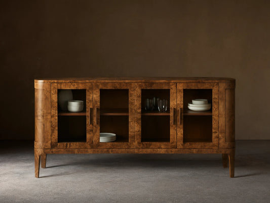 Front view of the mappa burl wood Mogadore Sideboard. Four glass doors, brass handles. Shelves display white bowls and glasses.